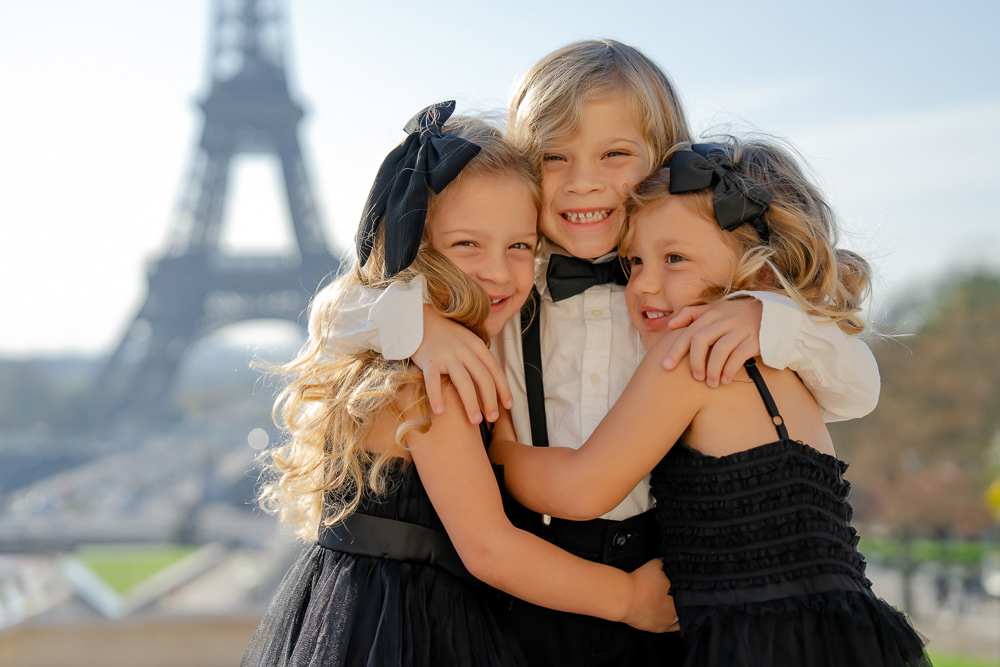 3 little siblings hugging for a cute family photo in front of the Eiffel Tower in Paris