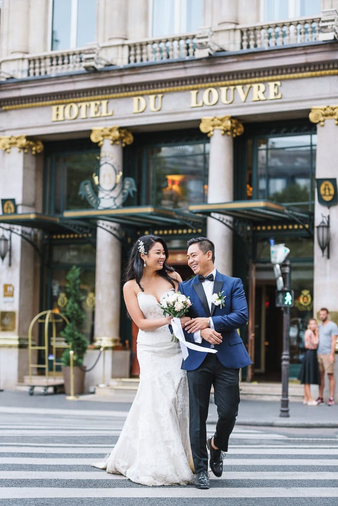 asian bide and groom crossing the street in front of the hotel du louvre in paris