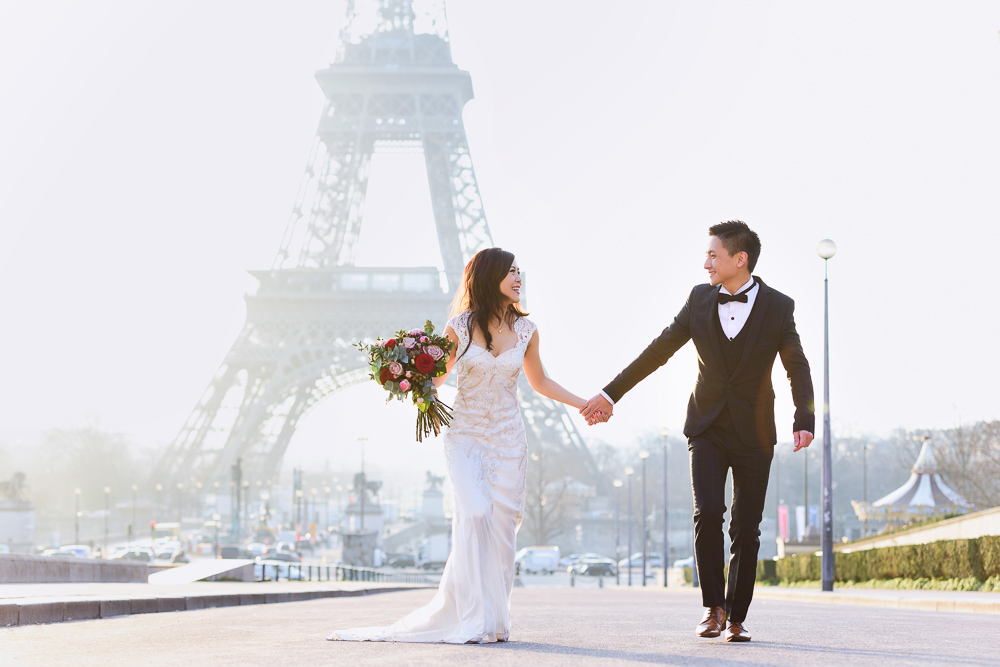 Asian bride and groom running hand in hand near Trocadero fountains