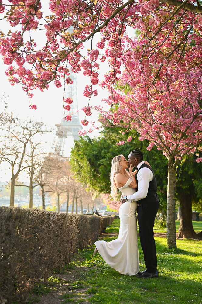 Couple dressed elegantly kissing under a chery blossom at the Eiffel Tower in Paris by Irene