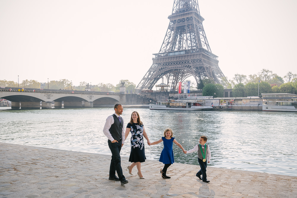 Cute family of 4 taking a stroll by the Seine River bank in front of the Eiffel Tower