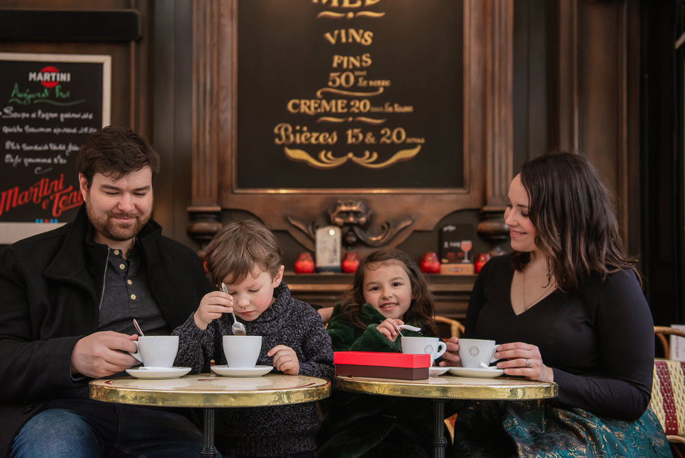 Family of 4 enjoying hot chocolate in a Parisian café during family photo session in Paris