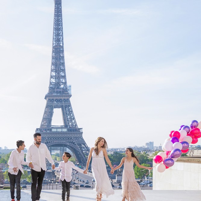 Family of 6 dressed in white posing for professional photographer Daniel in front of Eiffel tower with colorful balloons