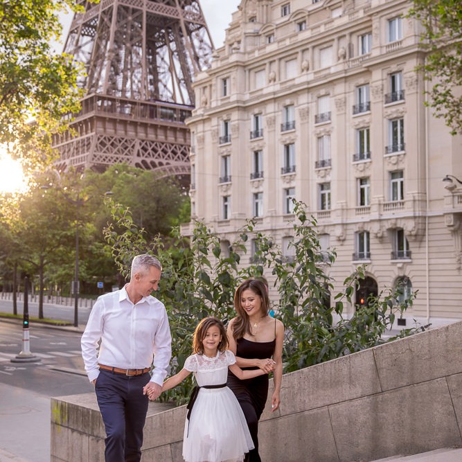 Family walking on stairs in front of the Eiffel Tower and Parisian buildings