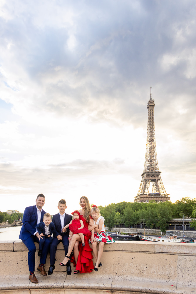 Family with 3 small kids posing in front of the Eiffel Tower in red and blue outfits