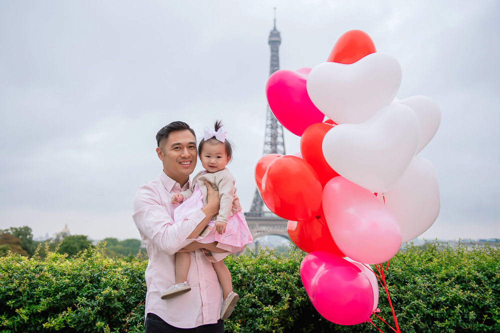 Father holding his daughter in his arms posing with a bunch of heart shaped balloons