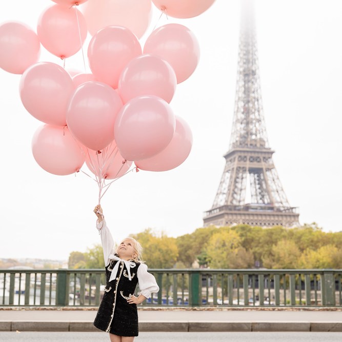 Little girl holding big bouquet of pink balloons posing for pictures in front of the Eiffel Tower