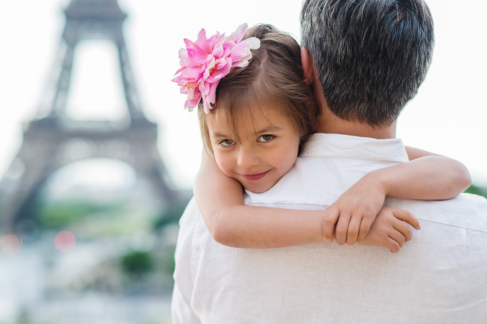 Little girl in her fathers arms looking back over his shoulder by the Eiffel tower