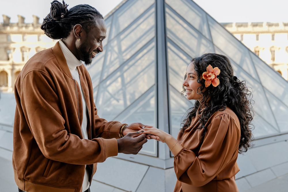 Man putting engagement ring on her girlfriends finger by the Louvre pyramid in Paris