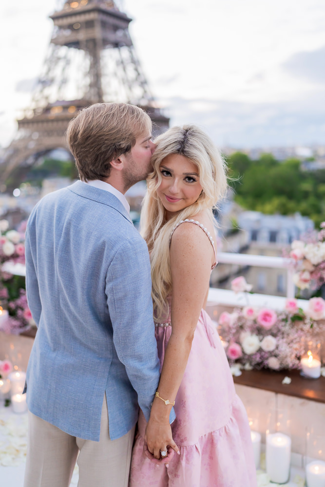 Newly engaged couple posing for professional photos on a private terrace overlooking the Eiffel Tower